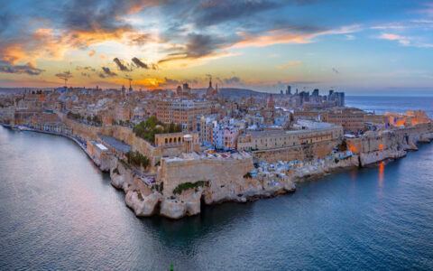 Aerial view of Valletta, Malta at sunset, with ancient brick walls running into the sea under a fiery sky.