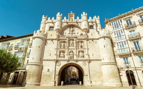 Santa maria arch in burgos that looks like a historic castle with small green trees on the ground on a sunny day