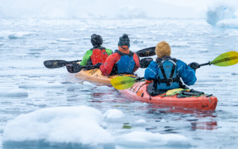3 kayakers on a Falklands, South Georgia & Antarctic Peninsula cruise paddle red & orange boats among iceberg bits in a snowstorm.