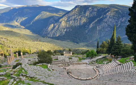 Aerial view of Delphi, Greece with amphitheater of stone sitting among green mountains on a partly cloudy day.