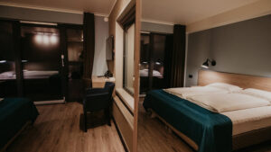 Guest room at Hotel Kria in south Iceland, with wall separating 2 double beds in white & teal, desk, wood floors & big windows.