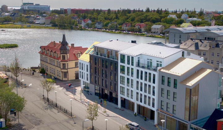 Hotel Reykjavik Saga exterior with white & gray walls, tall glass windows & modern look, beside the water on a sunny day.