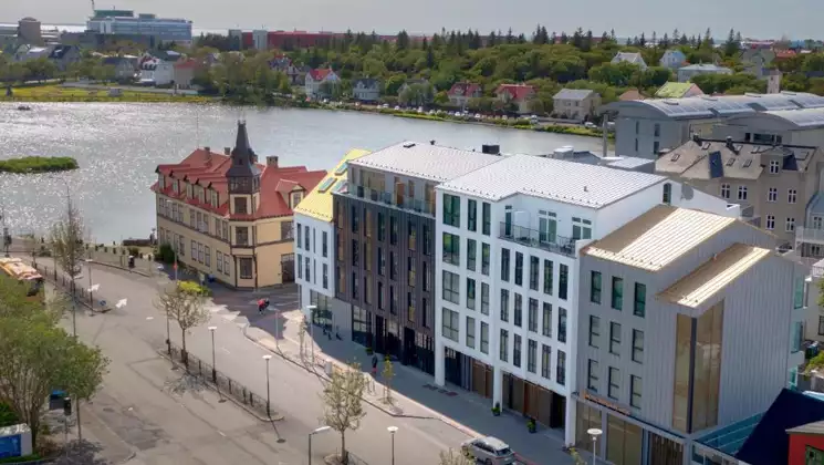 Hotel Reykjavik Saga exterior with white & gray walls, tall glass windows & modern look, beside the water on a sunny day.