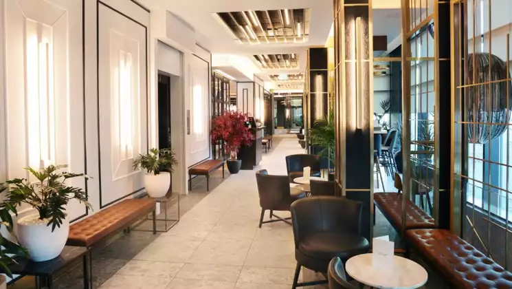 Bright hallway at Hotel Reykjavik Saga with tall windows, modern lighting, leather benches & chairs & small marble tables.