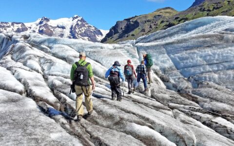 Travelers trek atop a dirty white & blue glacier on a sunny day during the Iceland Adventure: Land of Fire & Ice tour.