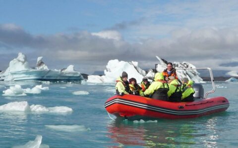 Group of Iceland Adventure travelers in dayglo green jackets Zodiac cruise among icebergs in calm water during a partly cloudy day.