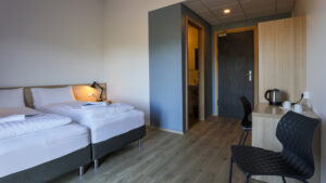 Guest room at Iceland's Lilja Guesthouse looking towards entry door with chair, 2 single beds, desk, tea kettle & wardrobe.