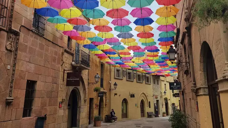 Canopy of colorful umbrellas on a historic stone street with beautiful archway doors on a sunny day.