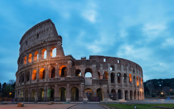 Coliseum in Rome Italy on a cloudy evening with lights shinning throughout the roman building.