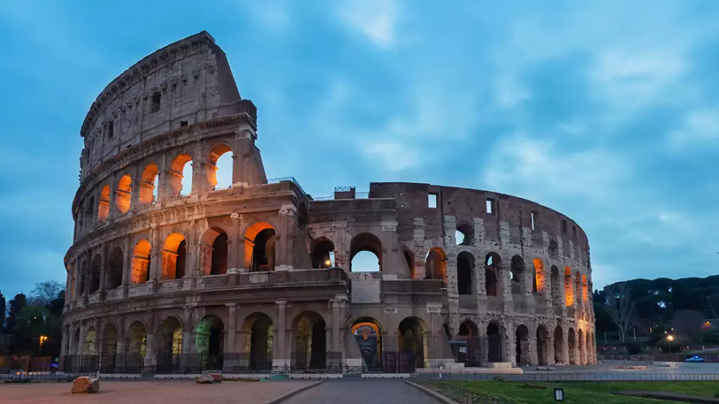 Coliseum in Rome Italy on a cloudy evening with lights shinning throughout the roman building.