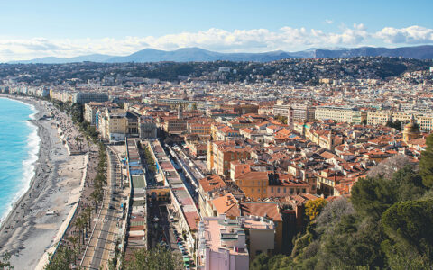 Scenic overlook of the city of Nice France with a bright blue beach and tan buildings on a sunny day.