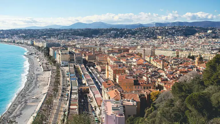 Scenic overlook of the city of Nice France with a bright blue beach and tan buildings on a sunny day.