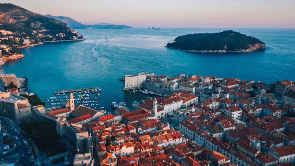 Aerial view of Dubrovnik, Croatia's seaside city with terracotta roofs, ancient walls & small harbor.