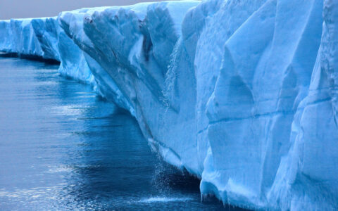 Close-up shot of blue Ross Ice Shelf where a section melts & creates a waterfall into dark sea on a winter day in Antarctica.