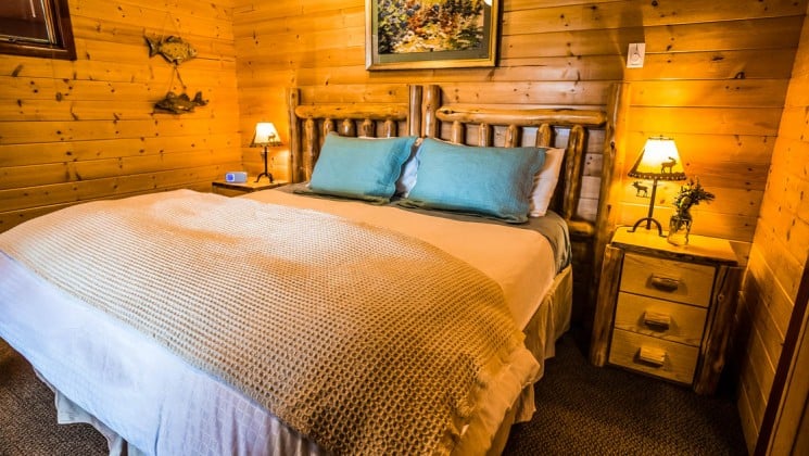 A queen-size bed in the Loon Suite with a wood interior, cozy decor, reading lamp, and nightstand, at the Tutka Bay Wilderness Lodge in Alaska