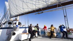 travelers standing on the deck of the Rembrandt van Rijn arctic small ship with the sail up on a sunny day