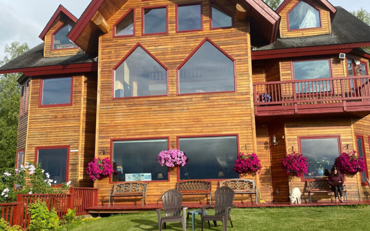 Exterior of Denali Overlook Inn with 3 floors, wood sideboards, multiple view windows, hanging flower baskets, deck & lawn.