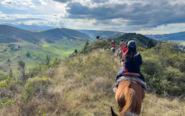 Line of Ecuador adventure tours travelers on horseback ride a ridge among green hills in the Andes highlands.