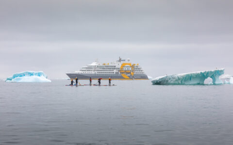 Stand-up paddleboarders pass icebergs near a luxury Antarctic expedition ship.