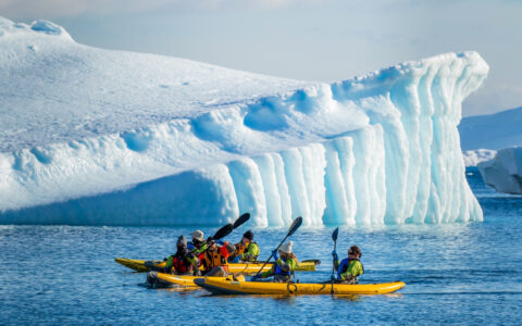 Travelers paddle beside a sculpted iceberg near the Antarctic Circle.