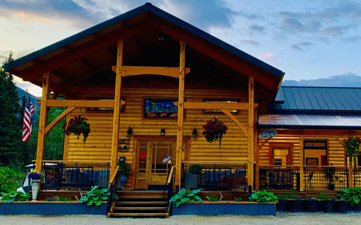 Exterior of large wooden cafe building with flowers & planter boxes beside wraparound deck, at McKinley Creekside Cabins.