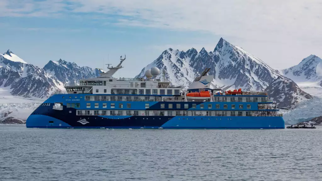 Exterior image of small ship cruise Antarctica with blue exterior in front of snowy mountains
