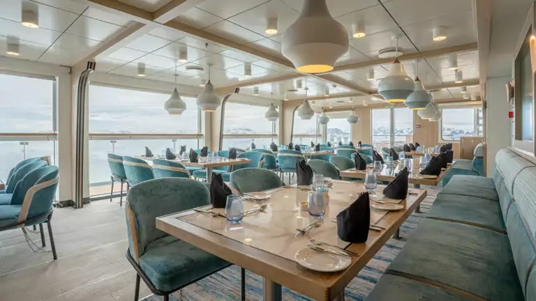 Dining area aboard small ship cruise with floor to ceilings windows and views of antarctica