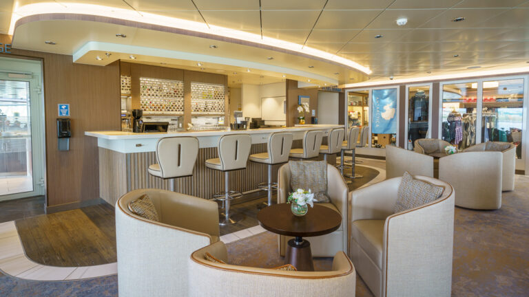 Latitude Bar on Ocean Explorer polar ship in gray & white with wood & stone decor, backed barstools & lounge chairs behind.