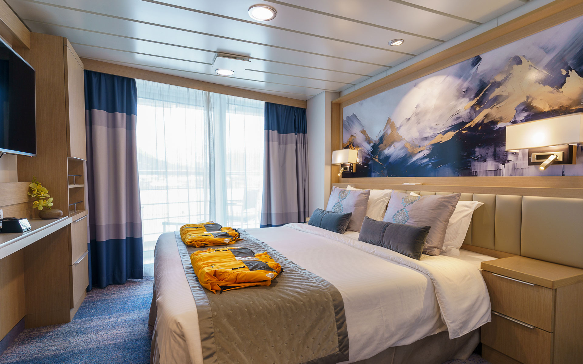 Deluxe Veranda Forward Stateroom on Ocean Explorer ship with double bed in white sheets, desk, map headboard & balcony.