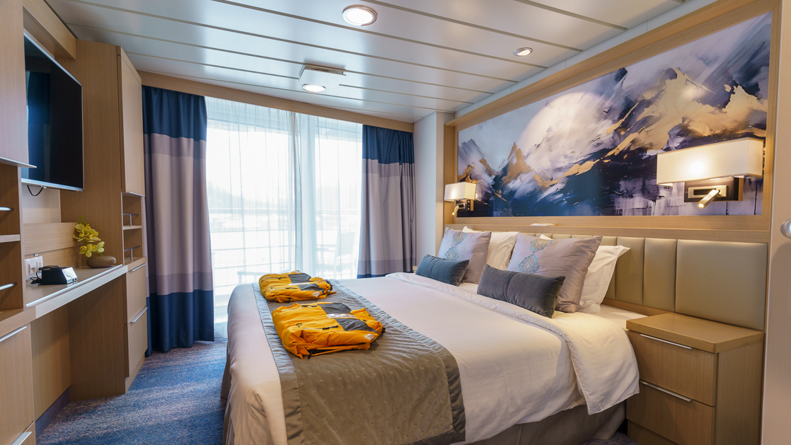 Deluxe Veranda Forward Stateroom on Ocean Explorer ship with double bed in white sheets, desk, map headboard & balcony.