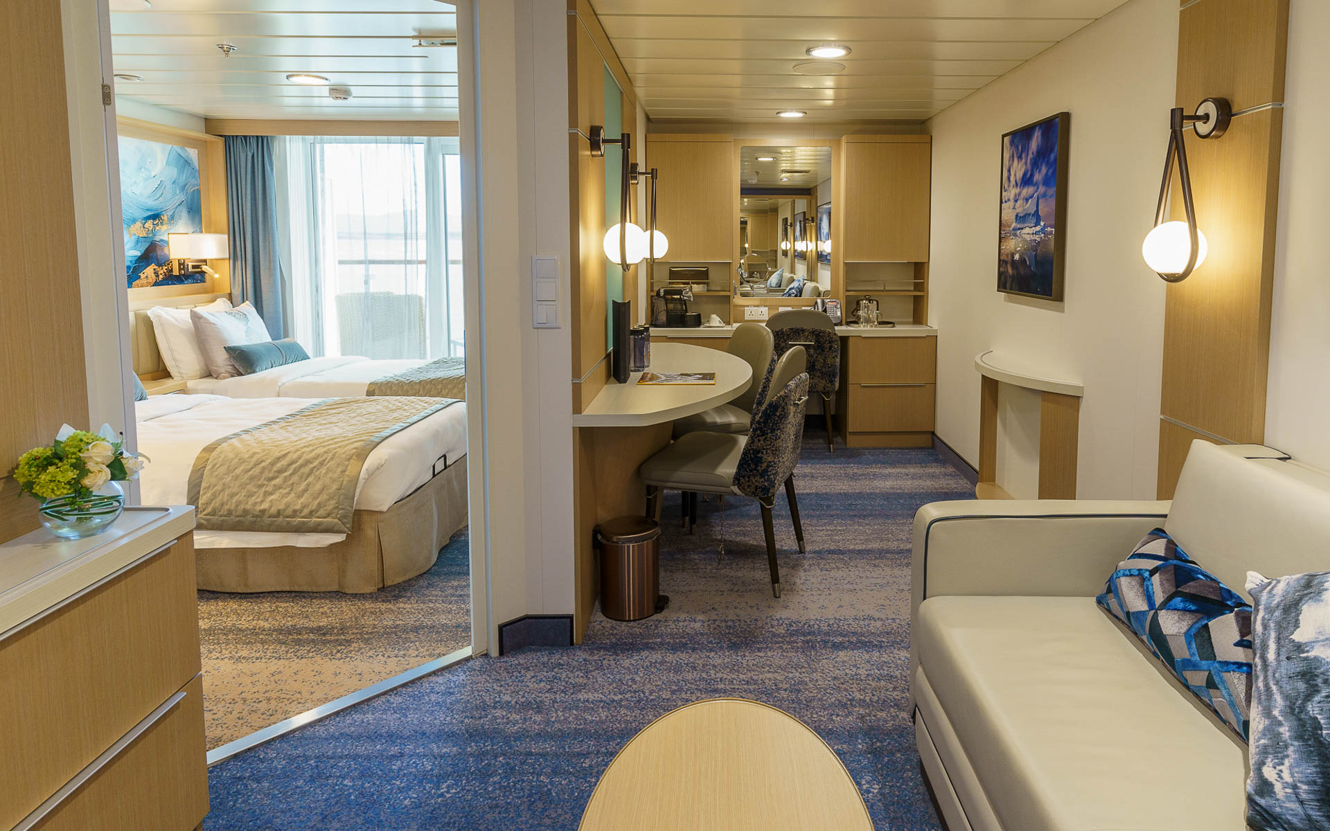Junior Suite second room in blue, gray & beige on Ocean Explorer ship with modern couch, wood coffee table, desk & photo art.