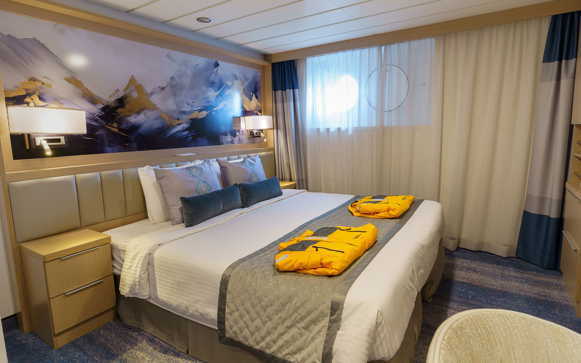 Studio Single cabin on Ocean Explorer ship with double bed in white sheets, desk, map headboard & 2 portholes.