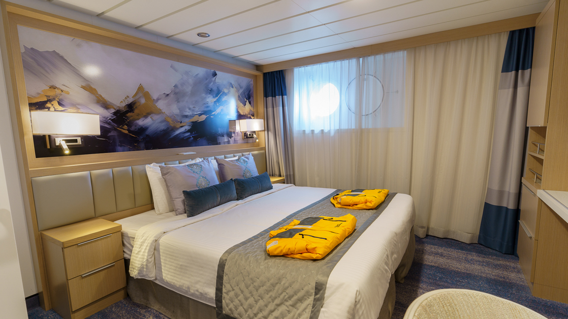 Studio Single cabin on Ocean Explorer ship with double bed in white sheets, desk, map headboard & 2 portholes.