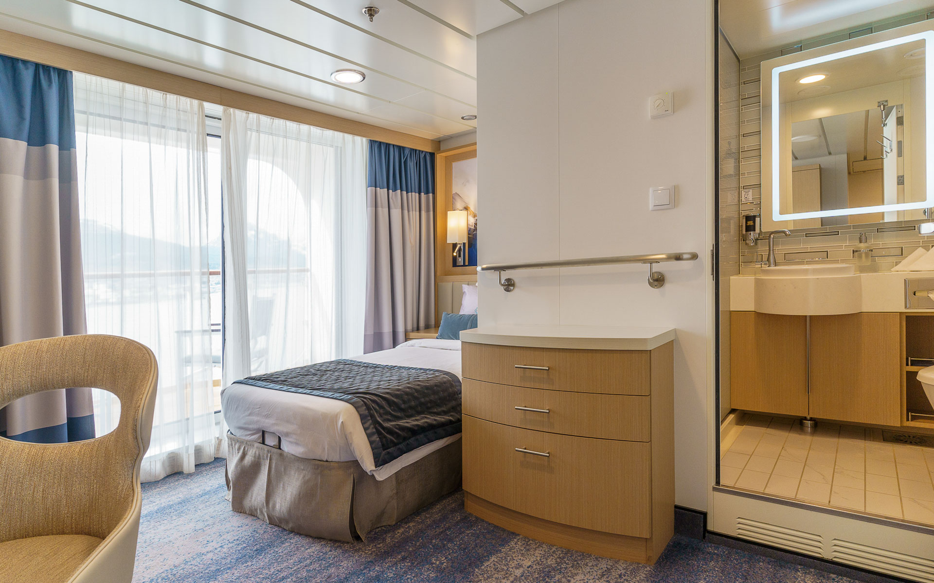 Studio Veranda cabin on Ocean Explorer ship with twin bed in white sheets, wood bedside table & dresser & map headboard.