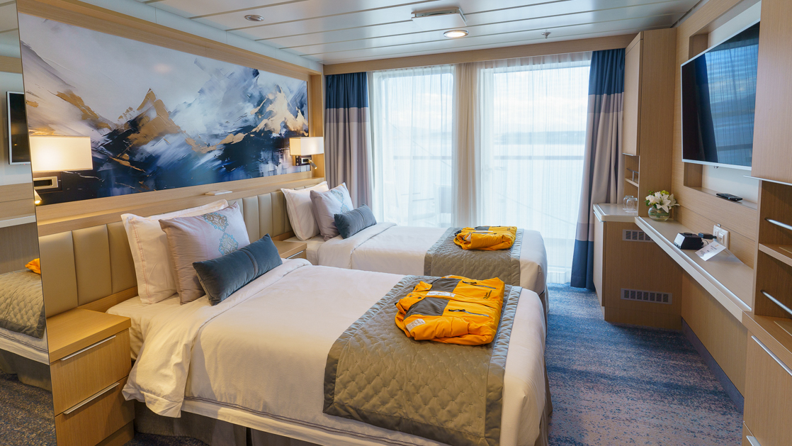 Veranda Suite on Ocean Explorer ship with twin beds in white sheets, desk, map headboard & balcony.