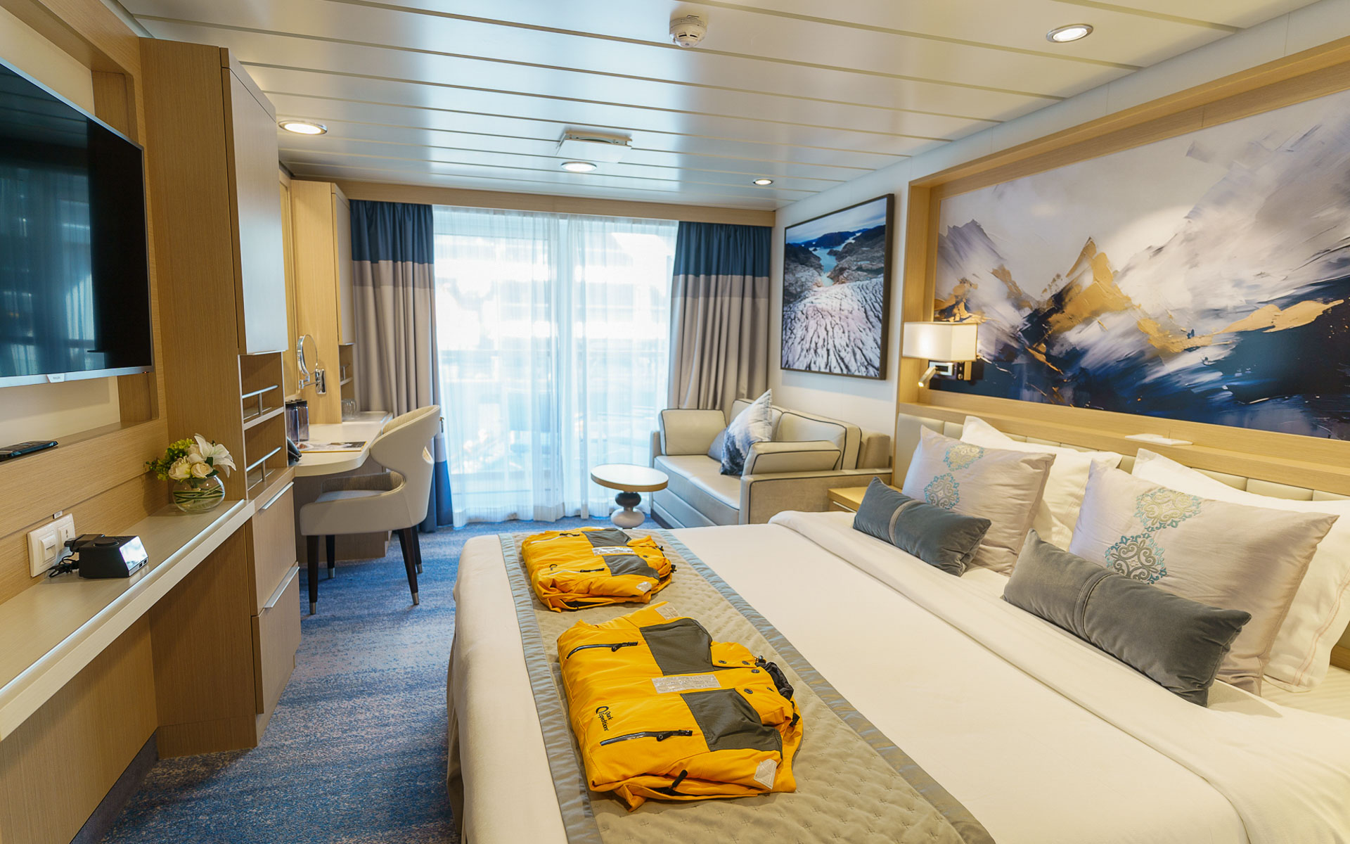 Veranda Suite on Ocean Explorer ship with double bed in white sheets, desk, map headboard & balcony.