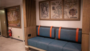 Renovated reception area on Ortelius ship with classic polar maps, modern blue bench seating, wood accents & beige floor.