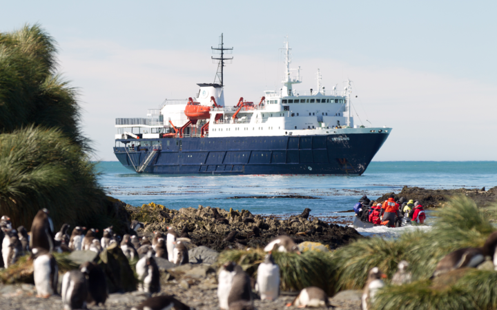 ortelius small ship cruising on a sunny day with penguins and travelers in the foreground