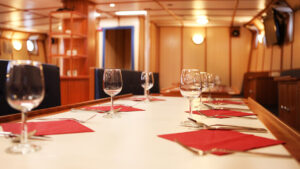 Rembrandt van Rijn small ship table set for dinner with silverware, red napkins & wine glasses.