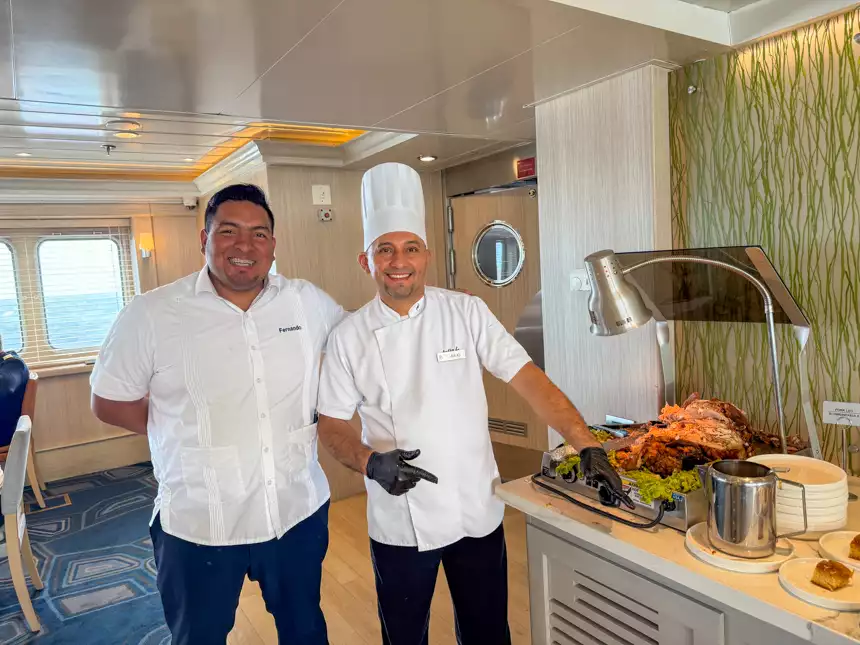 boat chefs smiling and posing for a picture in front of dinner being served behind them