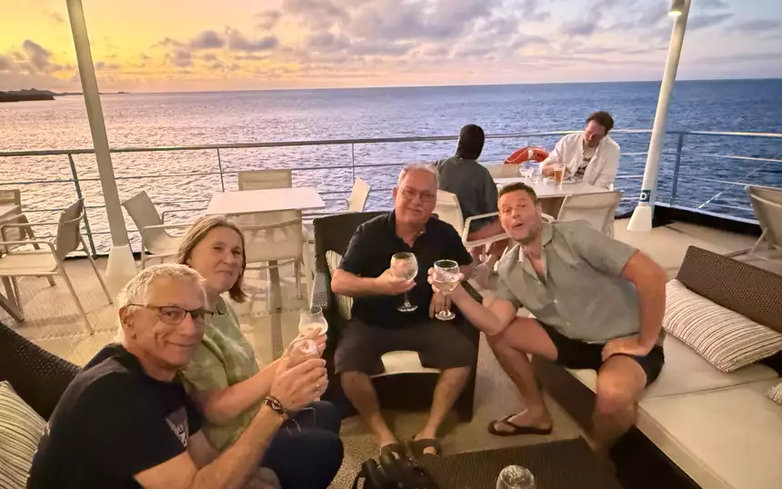 Guests enjoying a nice cocktail on the deck on their small ship cruise with a beautiful sunset behind them
