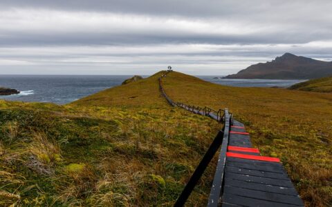 Wooden walkway painted black & red leads out to a silver statue at Cape Horn during the Essential Patagonia: Chilean Fjords & Torres del Paine Cruise.