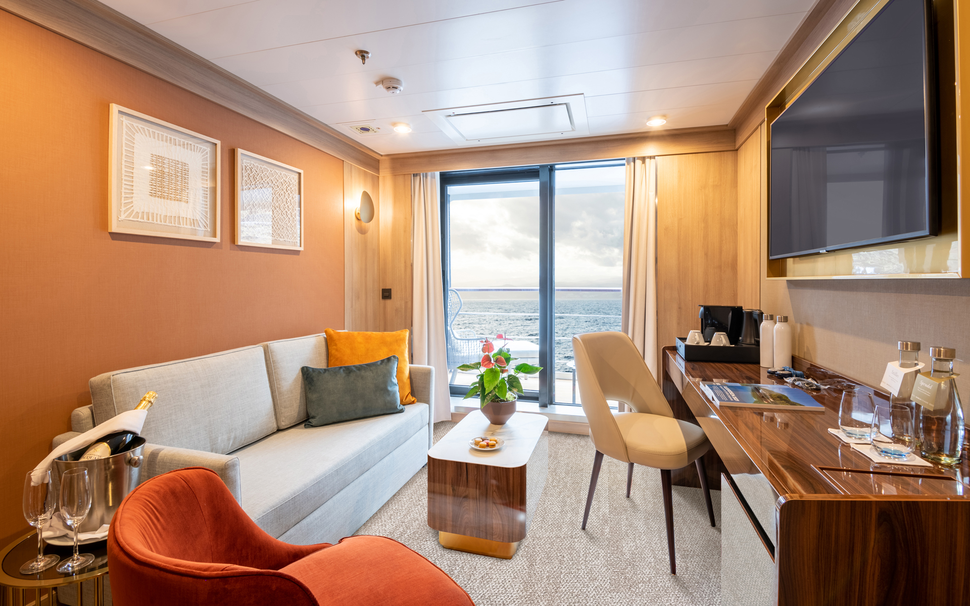 Second room of Deluxe Suite on World Voyager cruise ship with couch, coffee table, big desk, TV & sliding doors to balcony.