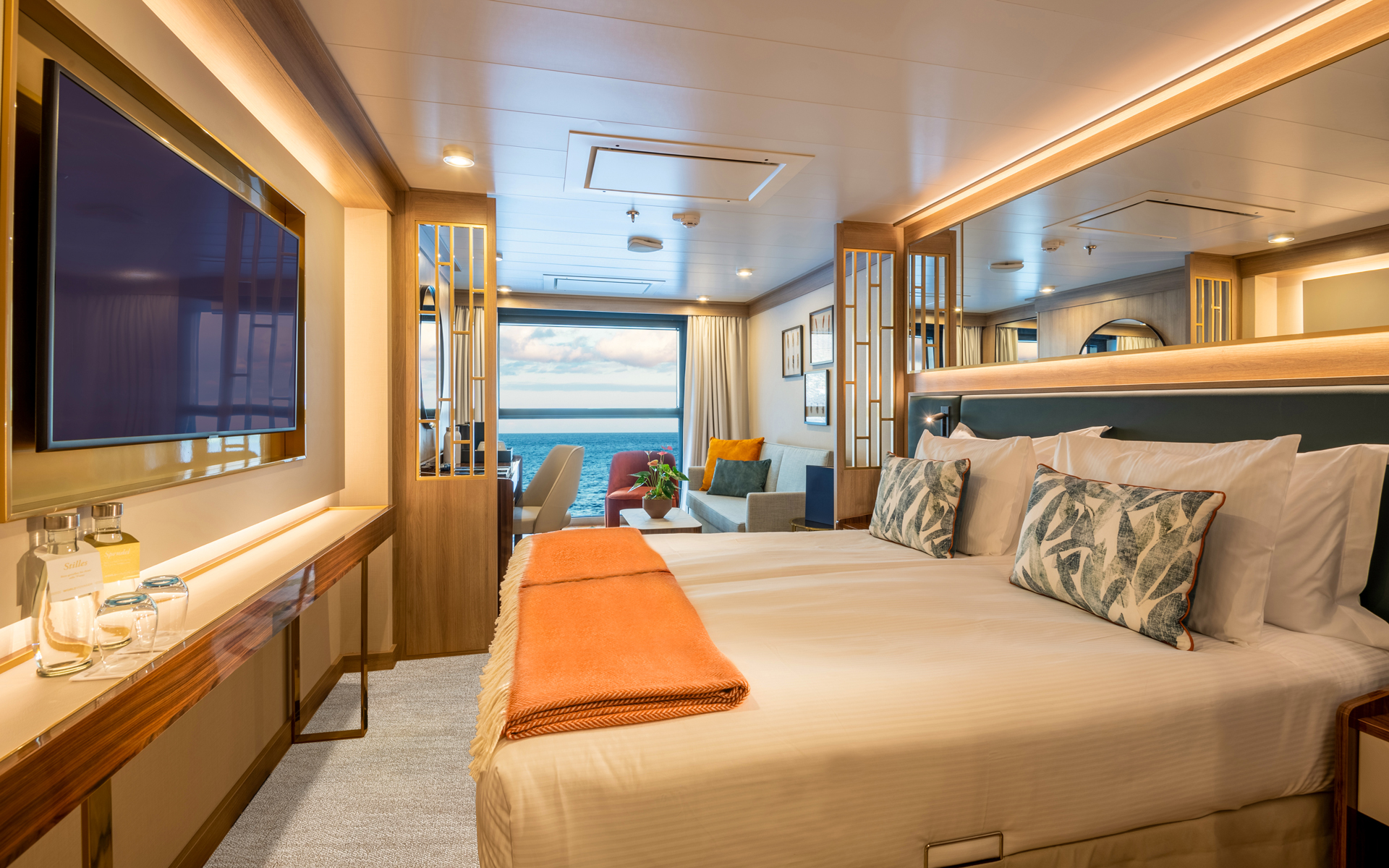 Infinity Suite on World Voyager cruise ship with double bed in white & peach linens, sitting area, desk & Juliette balcony.
