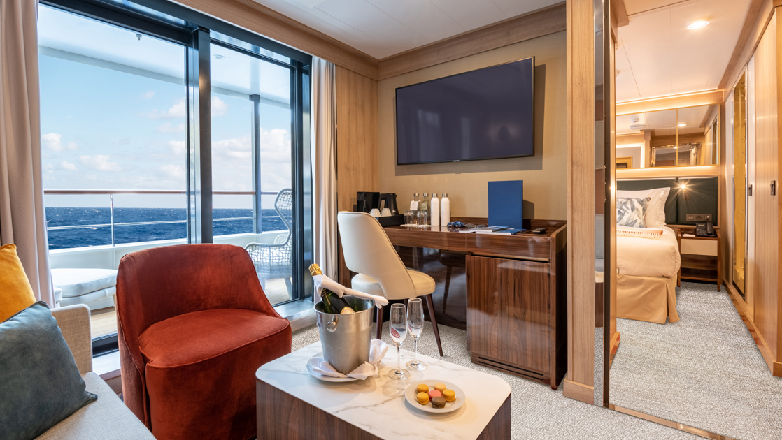 Owner's Suite on World Voyager cruise ship with large step-out balcony, separate sitting room with couch, desk & TV & bedroom.