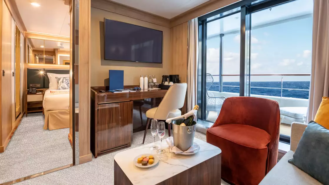 Superior Suite on World Voyager cruise ship with large step-out balcony, separate sitting room with couch, desk & TV & bedroom.