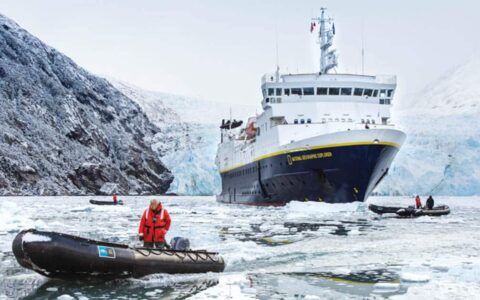 National Geographic small ship in front of glacier and two skiffs in front surrounded by ice in Garibaldi Fjord of Tierra Del Fuego Patagonia
