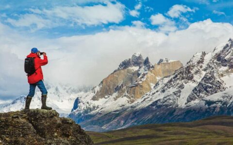 Hiker standing on rock and taking Photos of the snowy and jagged mountain landscape in Torres Del Paine National Park, Patagonia