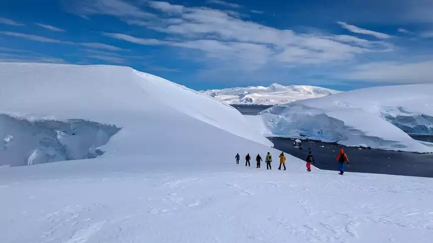 Mountaineers walk in a line on top of the icy snowy landscapes of Antarctica 