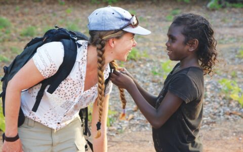 Woman traveler leans down to talk with a boy during a Cape York & Arnhem Land small ship cruise in northern Australia.